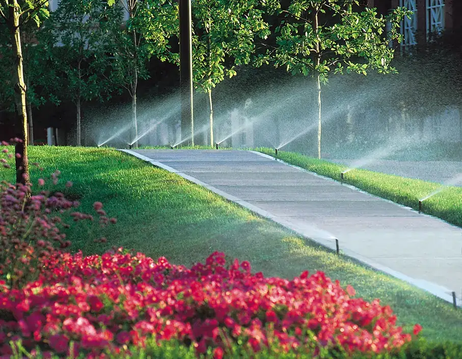 Sprinkler heads set along a garden pathway beside pink flowers