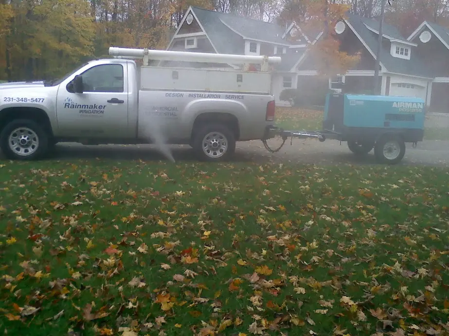 The Rainmaker truck and an air compressor trailer on a leaf-covered lawn during a fall blow-out