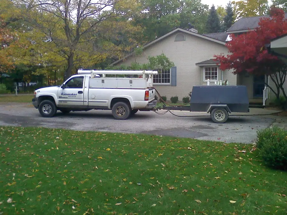 White Rainmaker Irrigation pickup towing an air compressor trailer in a Petoskey-area driveway in autumn